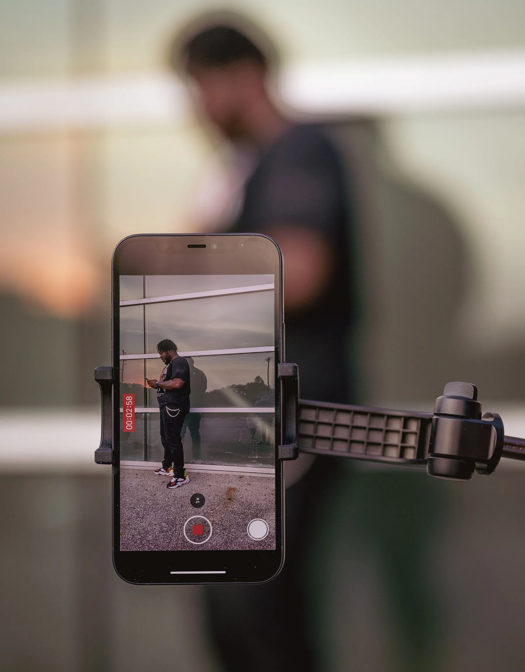 Hombre grabándose con un celular montado en un trípode frente a una pared de vidrio